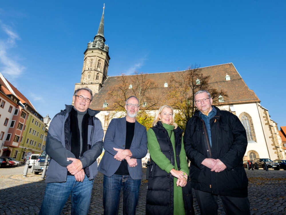 Gruppe von drei Männer und einer Frau, im Hintergrund ein Dom.