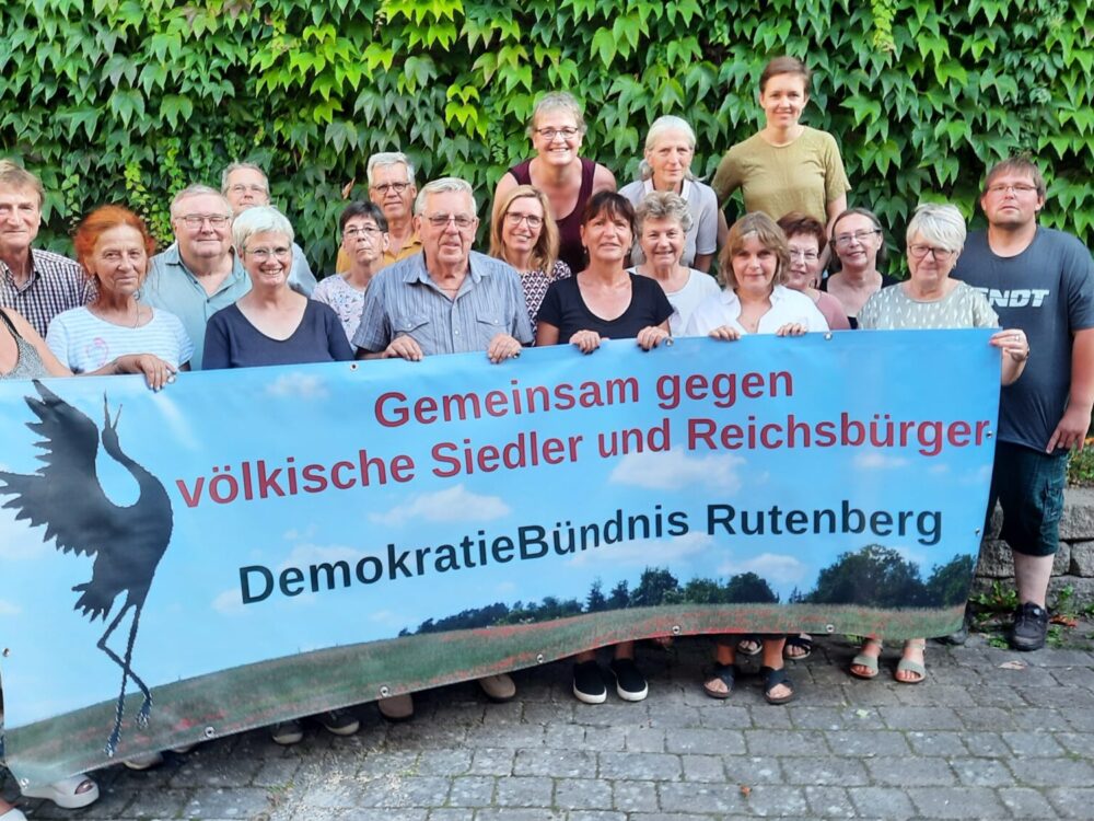 Menschengruppe vor einer begrünten Wand hält Plakat mit schwarzem Storch und Schriftzug in die Kamera.