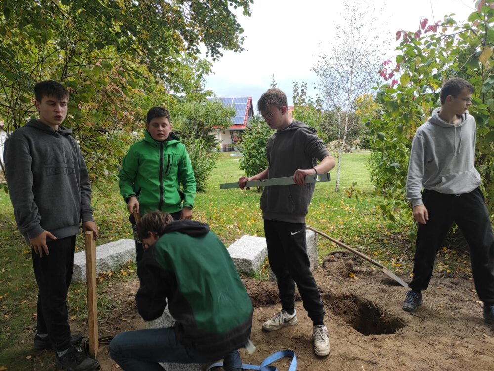 Jugendliche bei Arbeiten auf einer Wiese mit Schaufel, Holz, Stein und Wasserwaage.