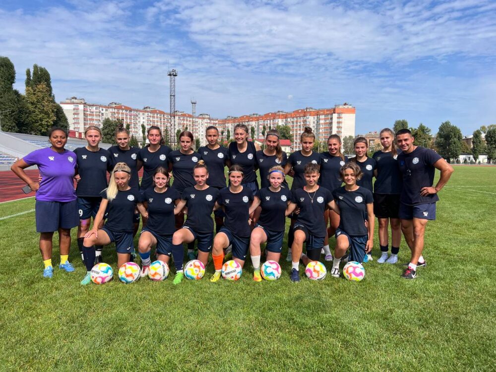 Spielerinnen des Fußballteams Mariupol stehen auf dem Rasen vor einem Häuserblock.