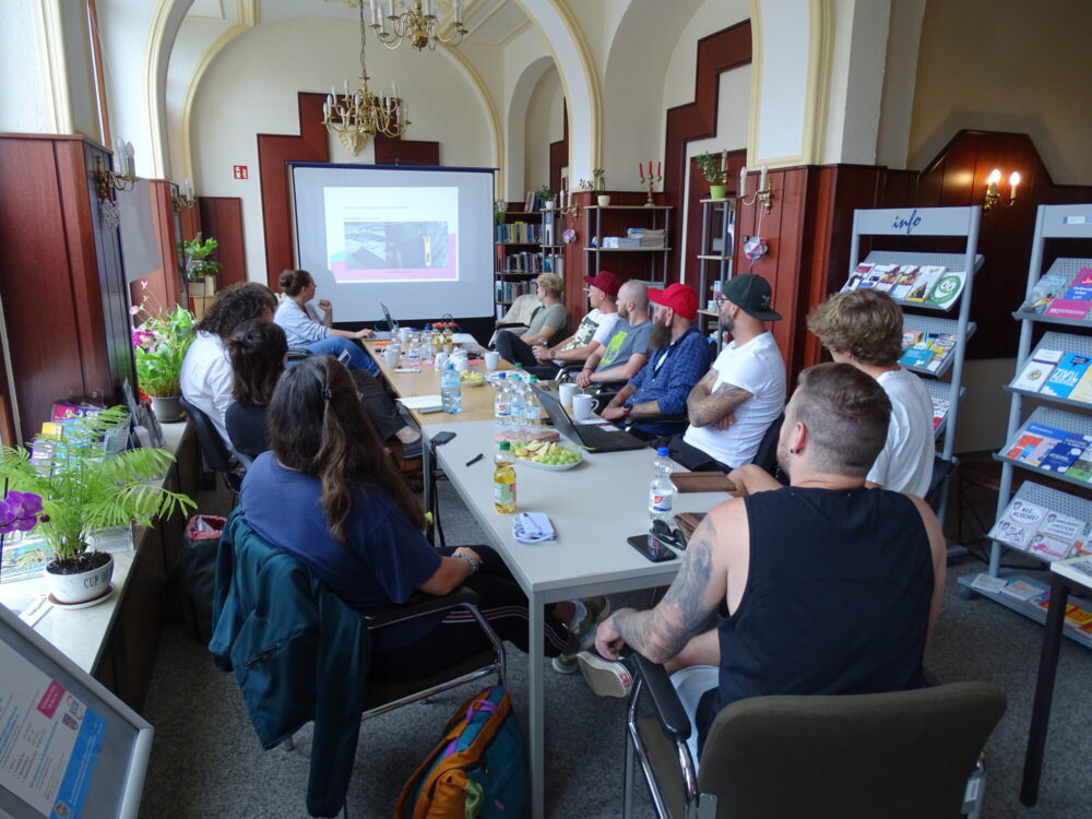 Menschen an einem Konferenztisch betrachten eine PowerPoint-Präsentation im Hintergrund, festlicher Raum im Alten Bahnhof Bad Schlema.