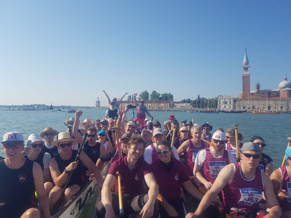 Paddler sitzend und jubelnd in Drachenbooten in der Lagune in Venedig, im Hintergrund Turm von S. Giorgio Maggiore.