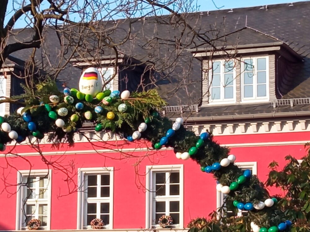 Festlich gestaltete Rankenbogen mit bemalten Ostereiern. Im Hintergrund ein rotes Haus.