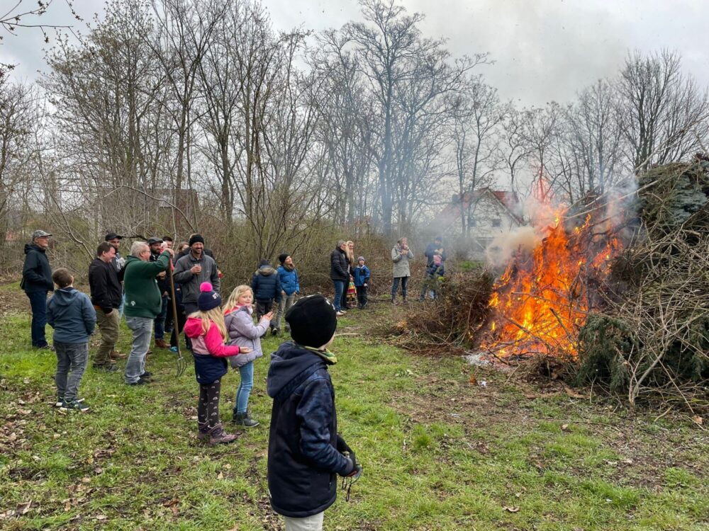 Kinder und Erwachsene in warmer Kleidung stehen um ein großes Feuer herum, das gerade angezündet wurde.