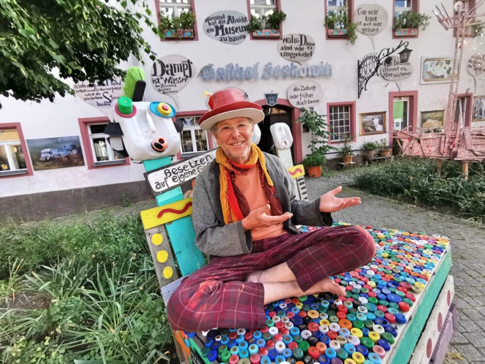 Der Betreiber des Lüseums in Radebeul sitzt fröhlich vor dem Ausstellungsgebäude und bittet die Besucher herein.