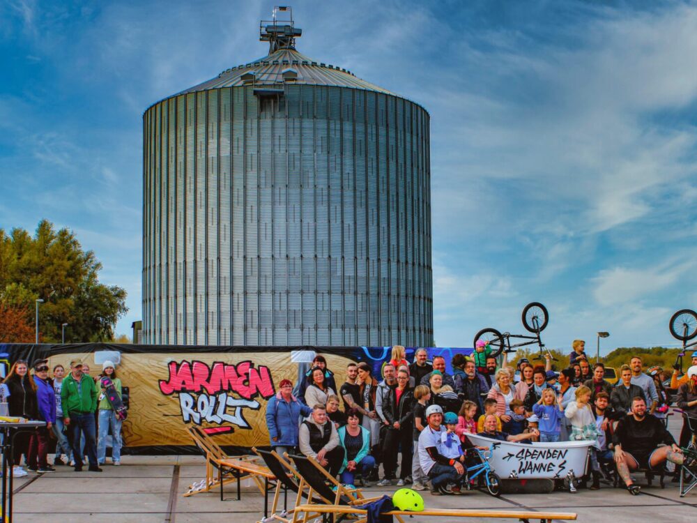 Zahlreiche Jugendliche mit BMX-Rädern vor einer Grafittiwand, im Hintergrund ein Silo.
