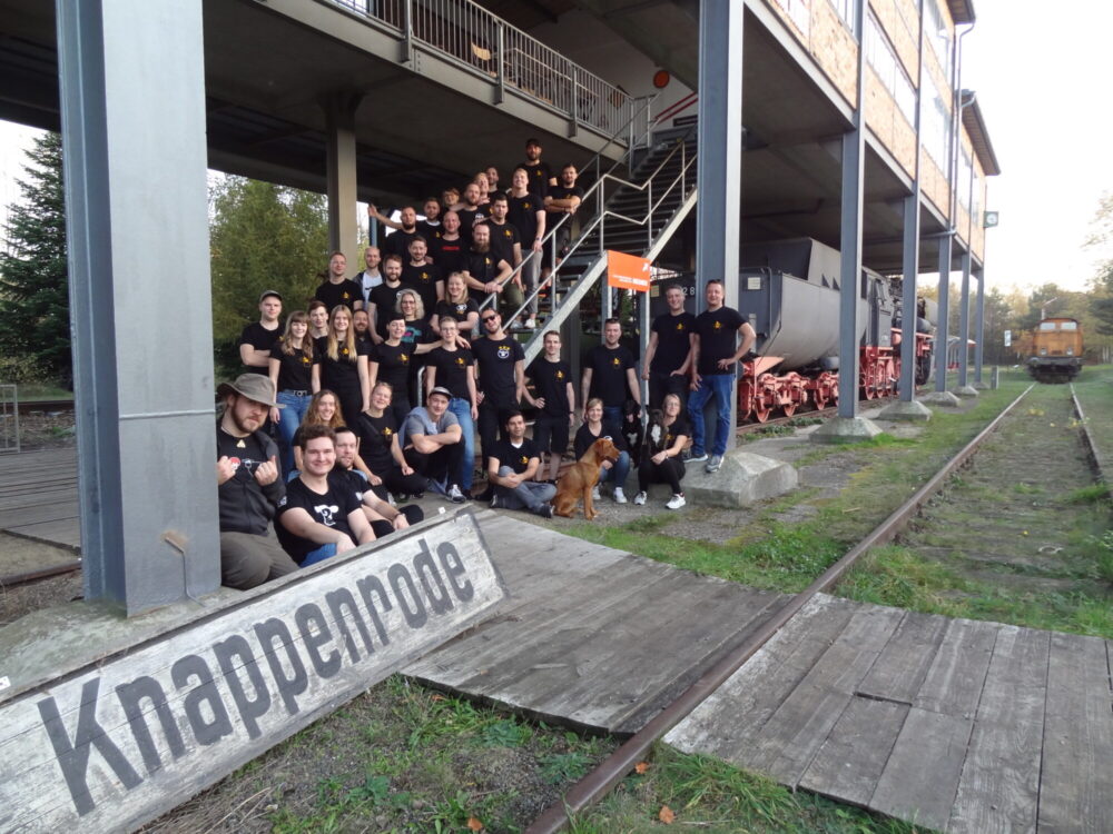 Gruppenfoto der Organisatoren Stroga Festival e. V. Knappenrode vor bergbaulichen Gebäuden mit Lokomotive im Hintergrund.