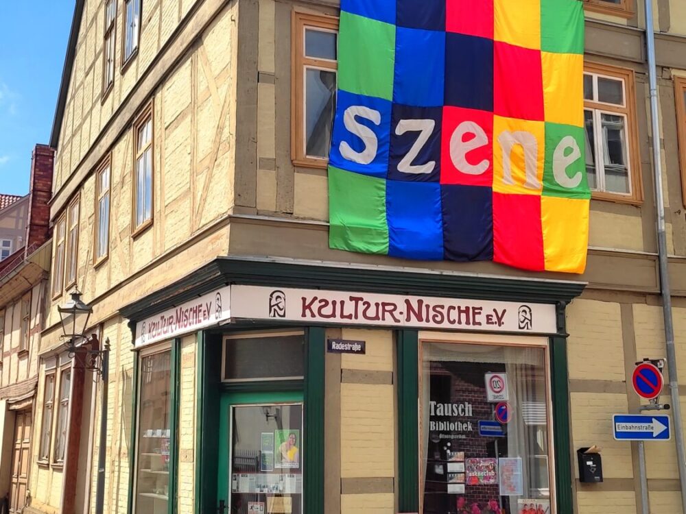 Hausecke mit einem bunten Banner, Schriftzug Szene, an der Hauswand.