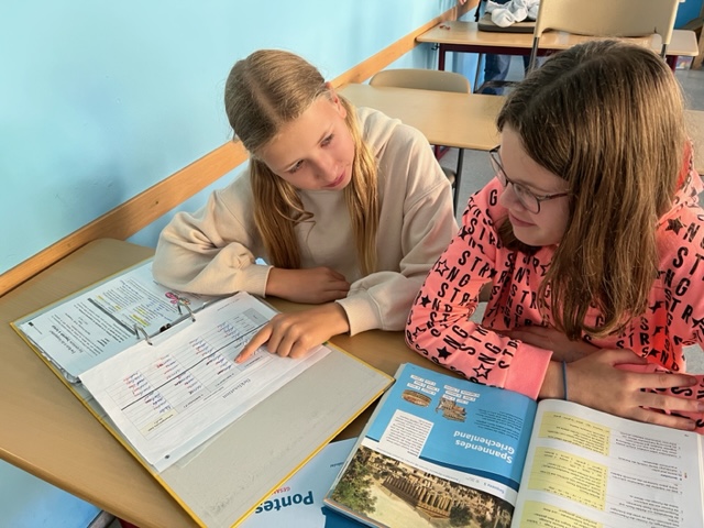 Zwei Schülerinnen sitzen auf der Schulbank und lernen gemeinsam.