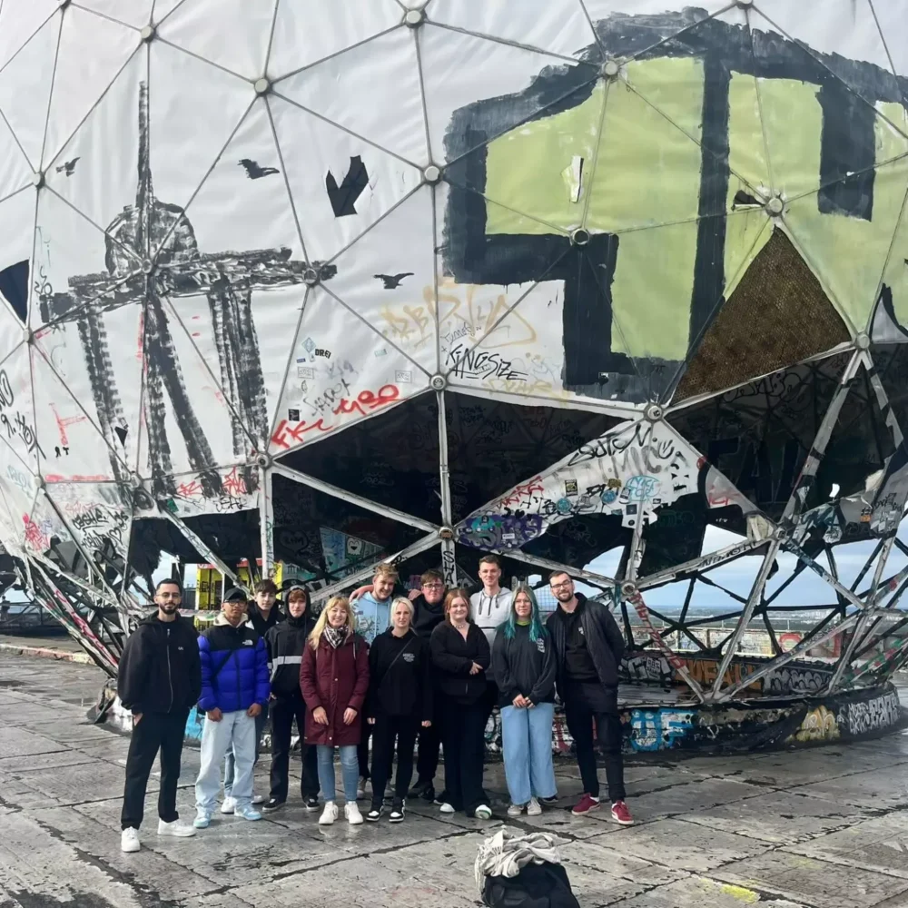 Neun Personen stehen vor einem großen, mit Graffiti beschmierten Kuppelbau im Freien.