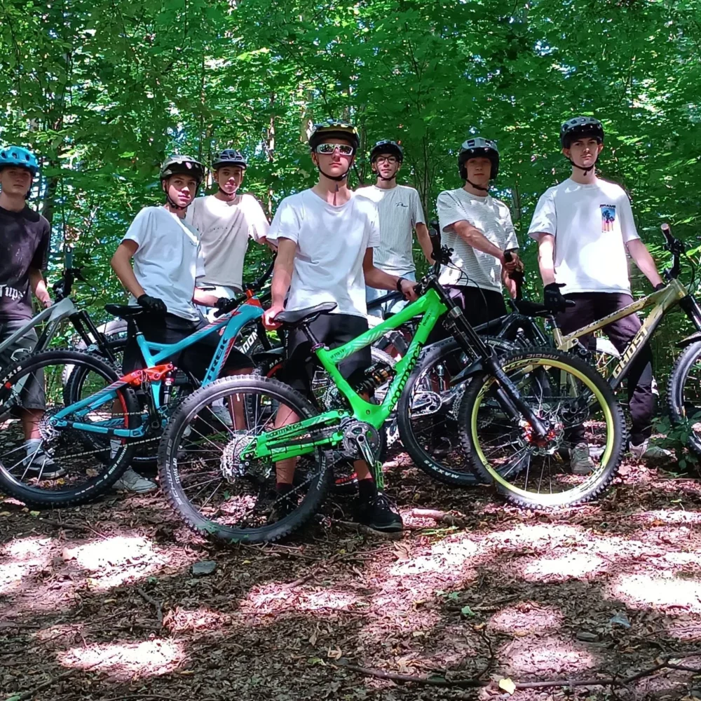 Sechs Personen mit Mountainbikes stehen zusammen in einem sonnenbeschienenen Waldgebiet.