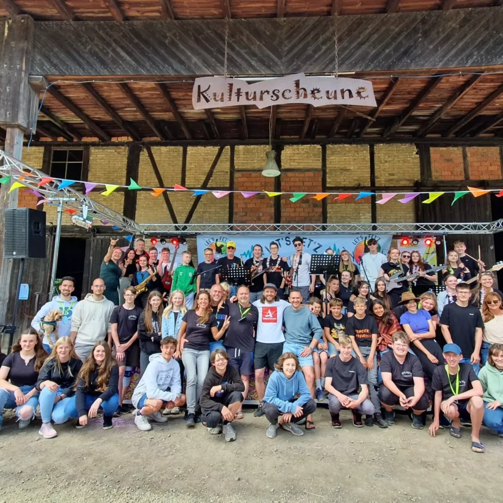 Eine große Gruppe von Menschen posiert für ein Foto vor einer Scheune mit einem Kulturscheune-Schild.